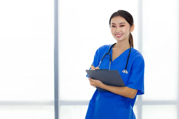Portrait of attractive Asian medical staff is standing and smiling while holding a clipboard in her hands.