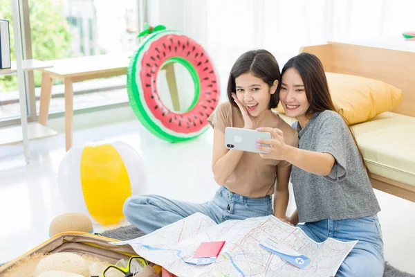 Two young Asian women enjoying taking selfie with mobile phones to update their status in online communities while resting at home.