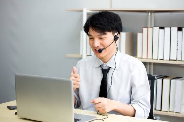 Asyalı bir erkek öğretmen ya da kulaklık takan bir öğretmen, öğrencilere evden bir dizüstü bilgisayarla video konferans sistemi üzerinden ders veriyormuş. Genç adam Webinar 'da meslektaşlarıyla buluşacak..