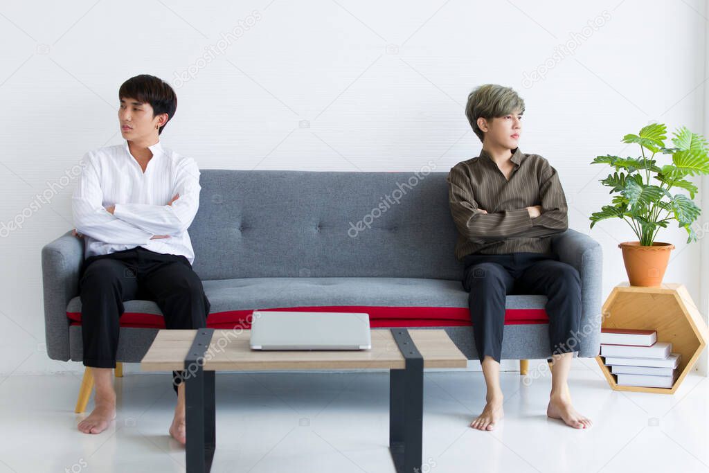 Asian male homosexual are bored and upset after quarreling. Gay couples are sitting on the sofa bed with arms crossed and don't look at each other. Both of their relationships come to an end.