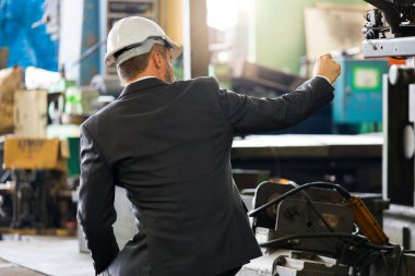 Fabrika müdürü üretim sürecine başlamadan önce makinelerin durumunu kontrol ediyor. Güvenlik standartlarını denetleyen bir mühendisin arka görüntüsü.