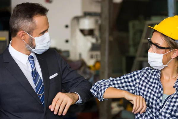 Industrial workers and factory managers greeting each other with elbows during the epidemic of COVID-19, Both of them were wearing masks to prevent the spread of infection.