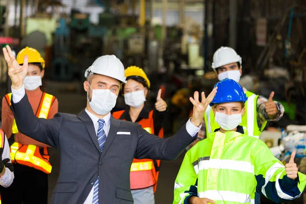 Group of factory worker wearing a surgical mask, They standing in front of the warehouse. The idea of working happily during a viral outbreak.