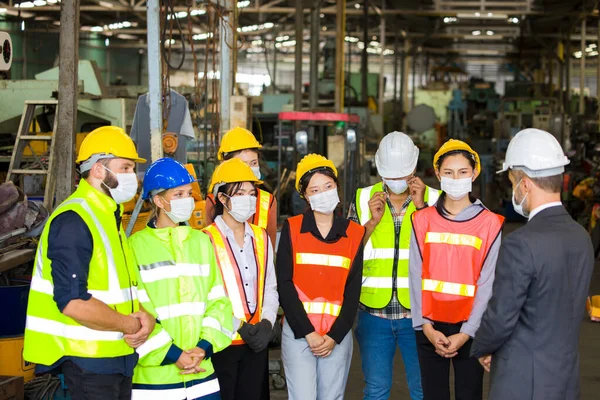 Group of Factory workers are meeting in the morning to plan the work each day at the warehouse with each person wearing a mask.