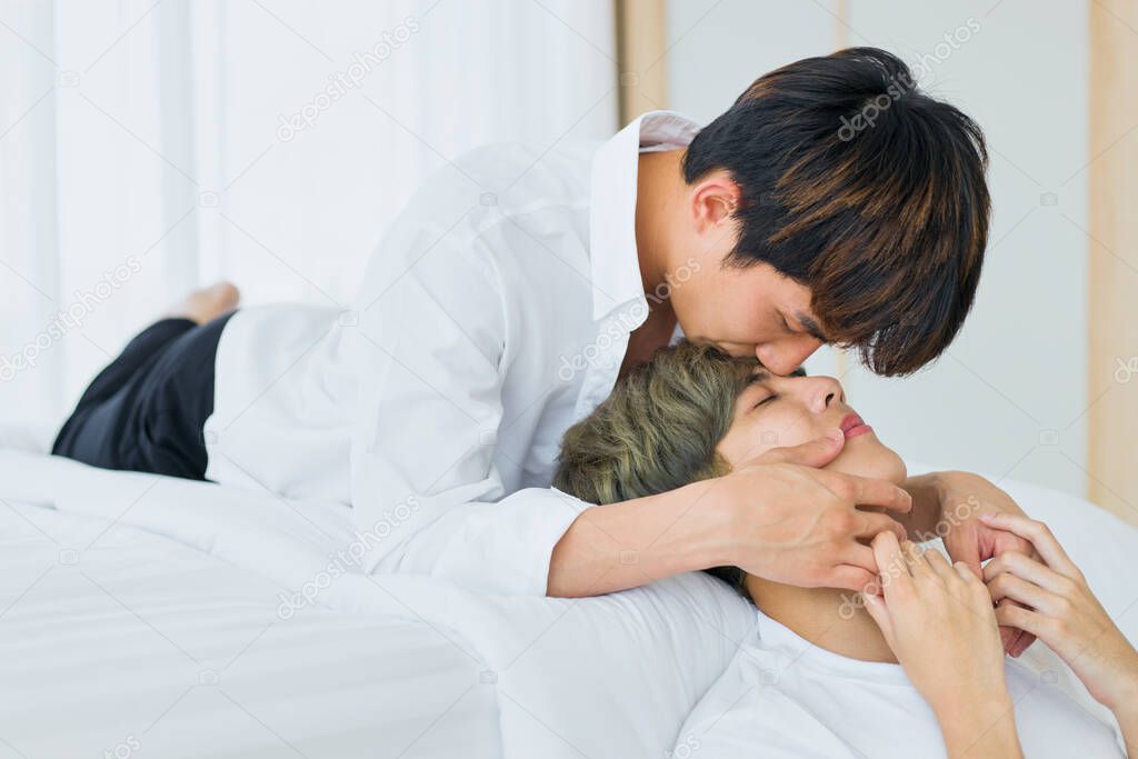 Happy Asian homosexual men or gay couples are lying on the white bed, Both of them are kissing contact together in the mood of love and attachment. Concept of LGBTQ pride.