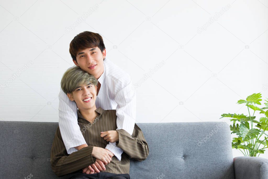 Happy Asian male homosexual or gay couples are sitting on the sofa bed, Both embrace each other with love and warmth and looking at the camera. Concept of LGBTQ pride.