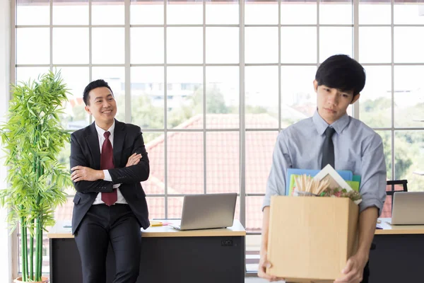 Asian Male employees fired from work, He is holding the box and walking out of the office because of a friend of bullying While a colleague showed signs of joy in the backside.