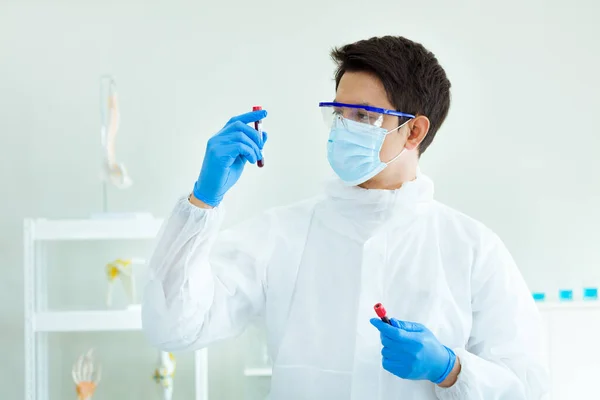 A medical technician is examining a blood sample in a laboratory. Scientists are holding a glass tube to experiment with chemical reactions.