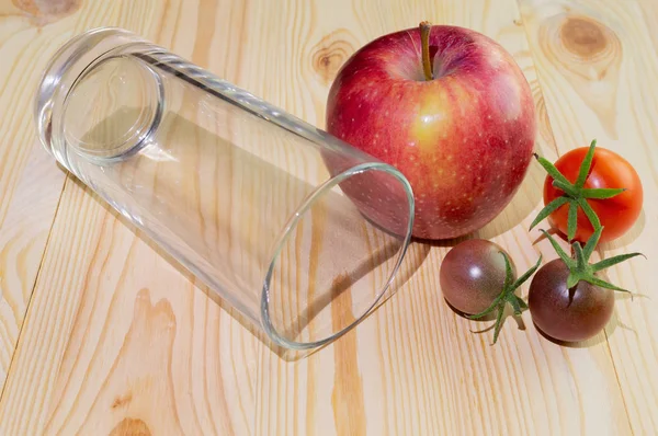 Domates ve elma ile ahşap bir arka plan üzerinde bir bardak suyu için boş cam