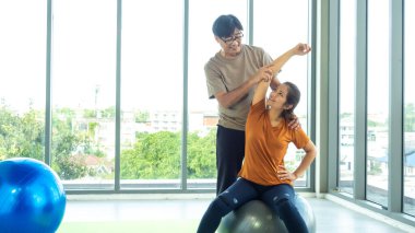 Koca, karısının doğru topta yoga yapmasına yardım ediyor. Vücudun en iyi etkinliği için, vücudu daha güçlü kılmak için..