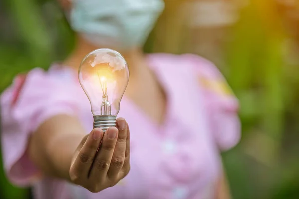 hand holding light bulb against nature, icons energy sources for renewable,