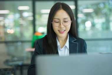 Asian businesswoman working at desk using laptop and notebook, talking with client or modern office building.