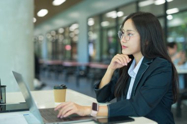 Asian businesswoman working at desk using laptop and notebook, talking with client or modern office building.