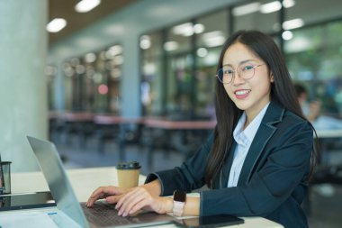 Asian businesswoman working at desk using laptop and notebook, talking with client or modern office building.