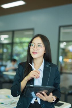 Asian businesswoman standing in front of modern business building and using tablet to work.