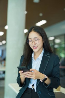 Asian businesswoman standing in front of modern business building and using tablet to work.