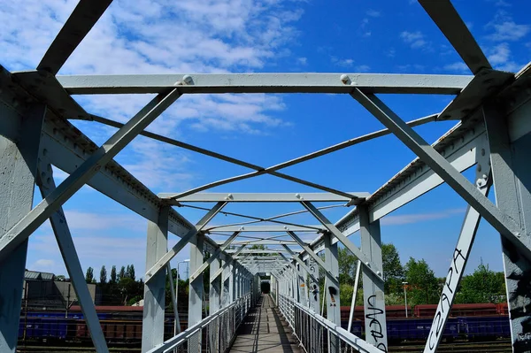 The metal structure of the bridge painted white against the sky with clouds.