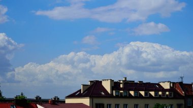 Mavi gökyüzü ve beyaz bulutlar güneşli bir günde renkli çatıların üzerinde.