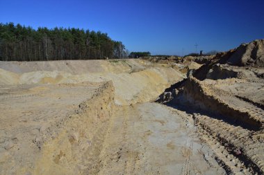 Gün ortası güneşinin keskin ışığında bir kum madeni. Ağaçların ufuklarında.