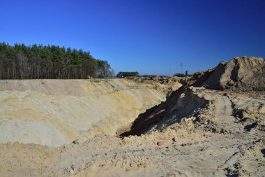 Gün ortası güneşinin keskin ışığında bir kum madeni. Ağaçların ufuklarında.