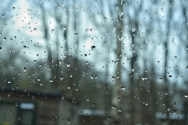 暗い日に窓ガラスに雨が降る 背景には 木々や家のぼやけたシルエット — ストック写真