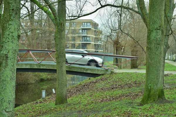 移動する車が運河の橋を渡って住宅や木々へと車を走らせます — ストック写真