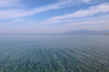Sakin, şeffaf, güneşli bir sabahın erken saatlerinde açık deniz manzarası, beyaz bulutlu mavi gökyüzü, güney İtalya 'da plaj tatili, Calabria