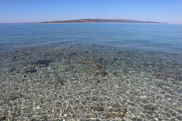 Hırvat sahilinde bir sahil. Açık gök mavisi suyun içinden ufuk çizgisinde Brach adasını görebilirsin.