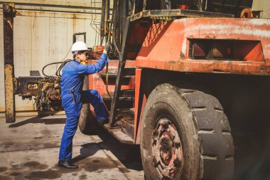 Erkek makine mühendisi kask takıyor, işe hazırlanıyor, depodaki kargo konteynerlerini taşımak için vinç kullanıyor ve dışarıda çalışırken güvenliği denetliyor..