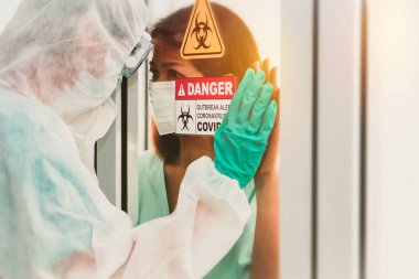 Enfeksiyon kapmış kadınlar Coronavirus (Covid-19) ve PPE koruyucu giysiler giyen genç adam arasındaki endişeler. Muhafaza odasında birlikte camdan bakıp tedaviyi yakından izliyoruz.