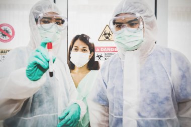 Endişeli bir kadın hasta gribi kontrol etmek için tıbbi bir ekibin elindeki kendi kan örneği tüpüne baktı. Coronavirus ya da COVID-19 salgını, enfeksiyonsuz güçlü sağlık umutlarıyla.