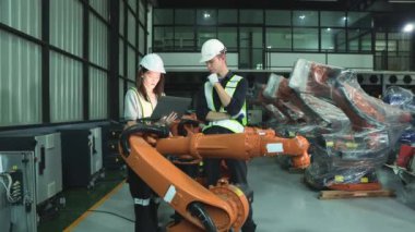 Erkek ve kadın elektrikçi robot mühendisi, depo modern iş sektörü 4.0 'da dizüstü bilgisayar elektronik otomasyon sistemi kurulumu ile yeni kaynak robotu test etme sürecini denetliyor.