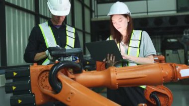 Erkek ve kadın elektrikçi robot mühendisi, depo modern iş sektörü 4.0 'da dizüstü bilgisayar elektronik otomasyon sistemi kurulumu ile yeni kaynak robotu test etme sürecini denetliyor.