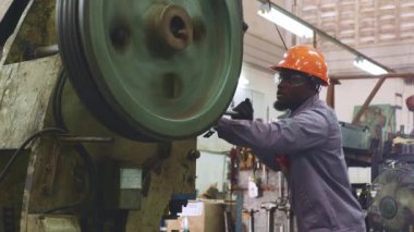 Siyah şapkalı Afrikalı erkek teknisyen, motor parçaları üreten bir fabrikada yüksek hızda dönen bir makara makinesinde dikkatlice çalışıyor..