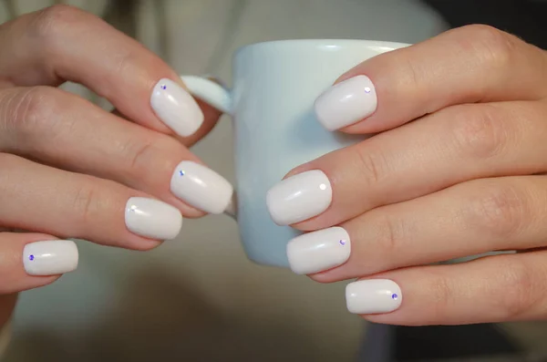 A Cup of espresso coffee in the hands of a young woman. Nails are covered with a light shade of gel Polish. Manicure ideas.