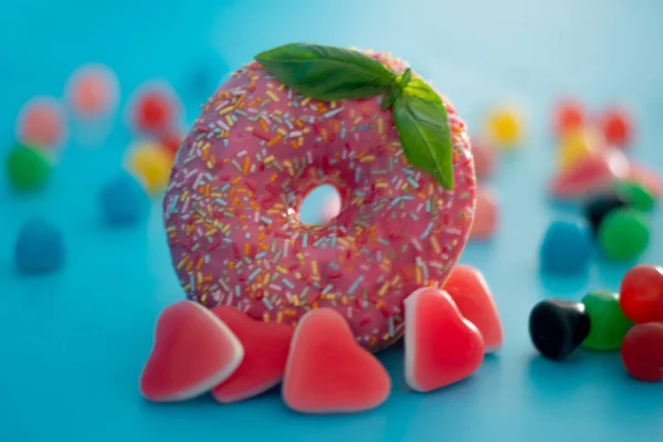 A pink doughnut and an ice cream with fruits and candy in a blue background