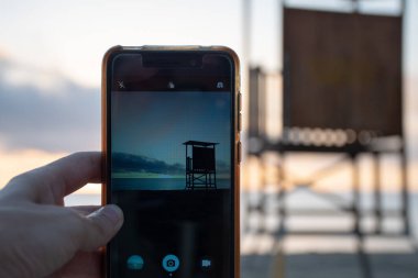 Gün doğumunda sahilde fotoğraf çeken bir kadın.