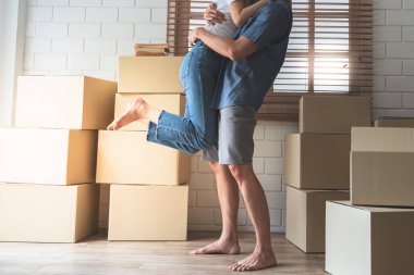 Hem mutlu olan hem de yeni bir eve taşınmayı kutlayan karısını kucağında taşıyan ve kucaklayan koca. Yerde kutular, aile ve gerçek taşınma konseptine sahip..