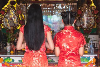 Kırmızı bir keongsam giyen Asyalı bir kadının sırtında Tanrılara saygılarını sunmak için bir türbede dikilirken Çin Yeni Yılı 'nda, insanlara ve tatil konseptine iyi şanslar dileyin..