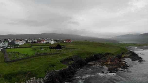 Luftaufnahme der Stadt auf den Färöer-Inseln, einem dänischen Territorium im Atlantik. Kirche, Friedhof und Häuser mit Gras auf dem Dach. — Stockvideo
