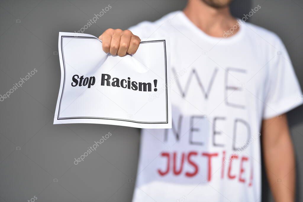 Man holds paper with words Stop Racism in front of grey wall. Black lives matter