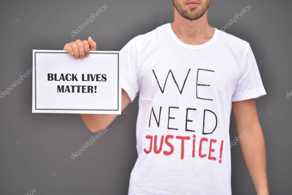 Man is holding paper with words Black lives matter in front of grey wall.