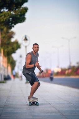 Gri elbiseli mutlu bir genç kaykay sürüyor ve Shaka işareti gösteriyor.