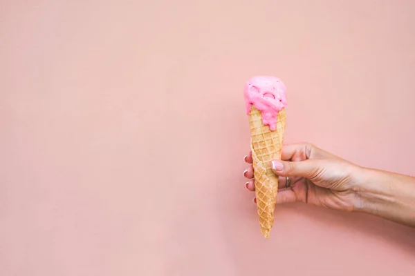 Girls hand holding melted pink strawberry ice cream cone on pink background.