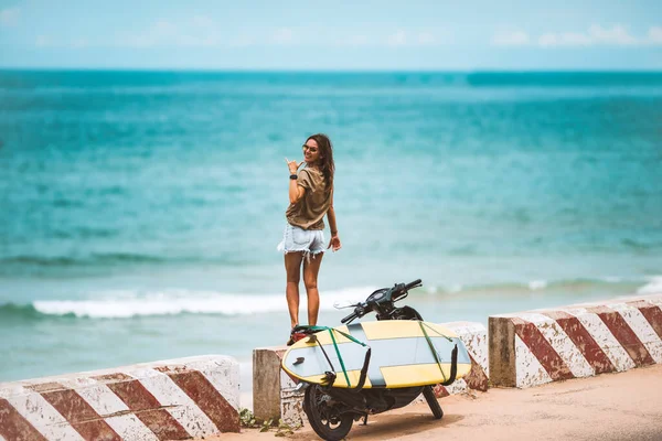 Felice ragazza surf sottile godendo la vita e mostrando segno shaka in vacanza estiva viaggiare nella giornata di sole vicino all'oceano e moto con tavola da surf longboard. Successo e concetto spensierato. — Foto Stock