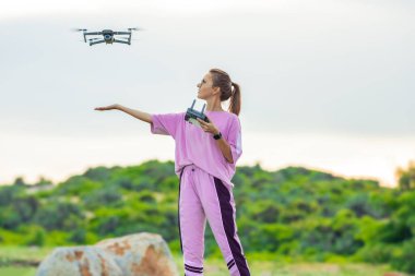 Pembe giysili genç bayan uzaktan kumandalı ve bir ele İniş Dronu tutuyor. Yazın insansız hava aracı dışarıda uçuyor.
