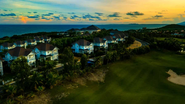 Aerial view or drone shot of villas compound development and golf at Mui Ne, Phan Thiet, Vietnam. Beautiful houses on sunset or sunrise with sea view.
