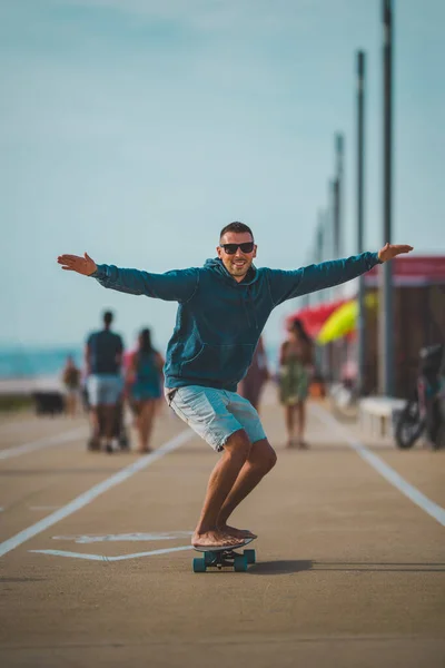 Gelukkig zorgeloos schaatser in een hoodie en zonnebril rijdt op een longboard. Zomer leuke activiteiten concept. — Stockfoto