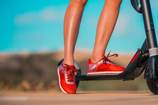 빨간 운동화를 신은 아름다운 다리를 가진 스포츠 여성이 전기 스쿠터를 들고 서 있는 모습이 눈에 띈다. 여름 야외 활동. — 스톡 사진