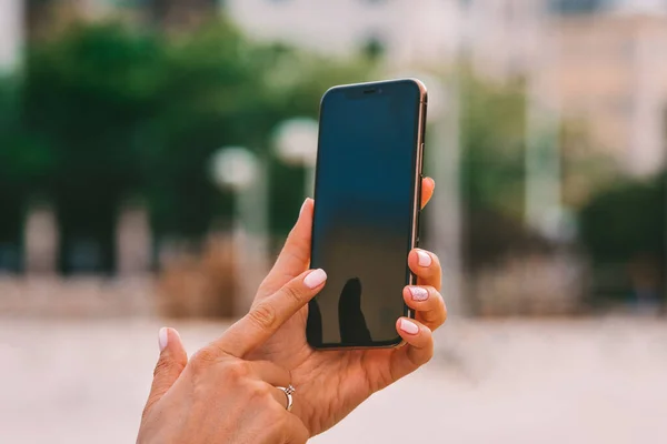 Primer plano de hermosas manos de las mujeres con la manicura rosa ordenada celebración de teléfono inteligente con pantalla negra. Mensaje de texto o uso de teléfono móvil para comprobar las redes sociales o dispositivo de desbloqueo — Foto de Stock